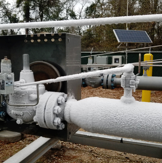 Frost-covered industrial pipe and valve assembly with solar panel in background
